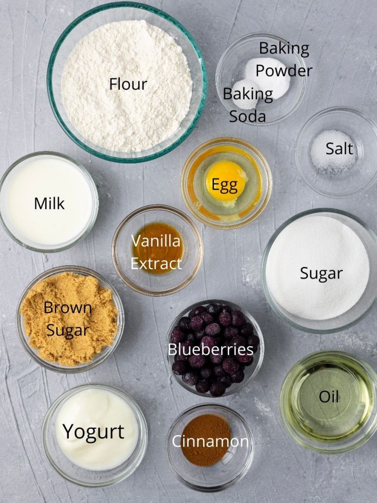 Ingredients needed to make muffins: flour, milk, egg, vanilla extract, baking powder and soda, salt, sugar, brown sugar, blueberries, yogurt, cinnamon, oil