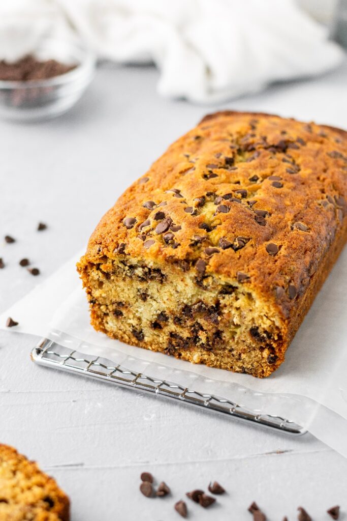 One banana banana bread with mini chocolate chips sitting on a parchment paper lined metal rack.