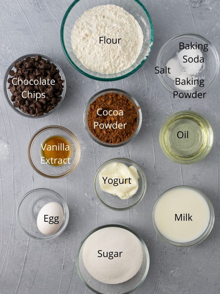 Ingredients needed for these muffins: flour, baking soda, baking powder, salt, cocoa powder, chocolate chips, oil, vanilla extract, yogurt, milk, sugar, and an egg