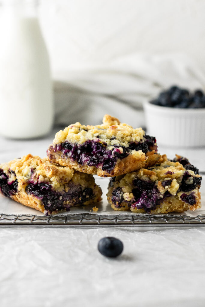 blueberry crumble bars stacked on a wire rack with a glass of milk