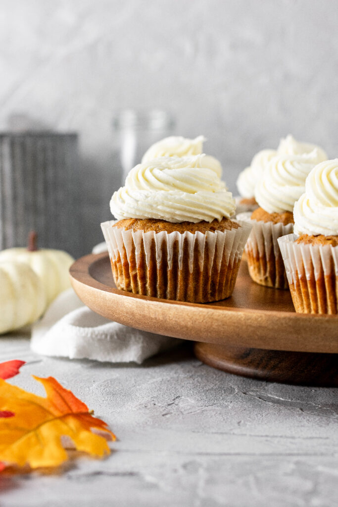 pumpkin cupcakes with maple buttercream sitting on top of a brown cake stand with leaves 