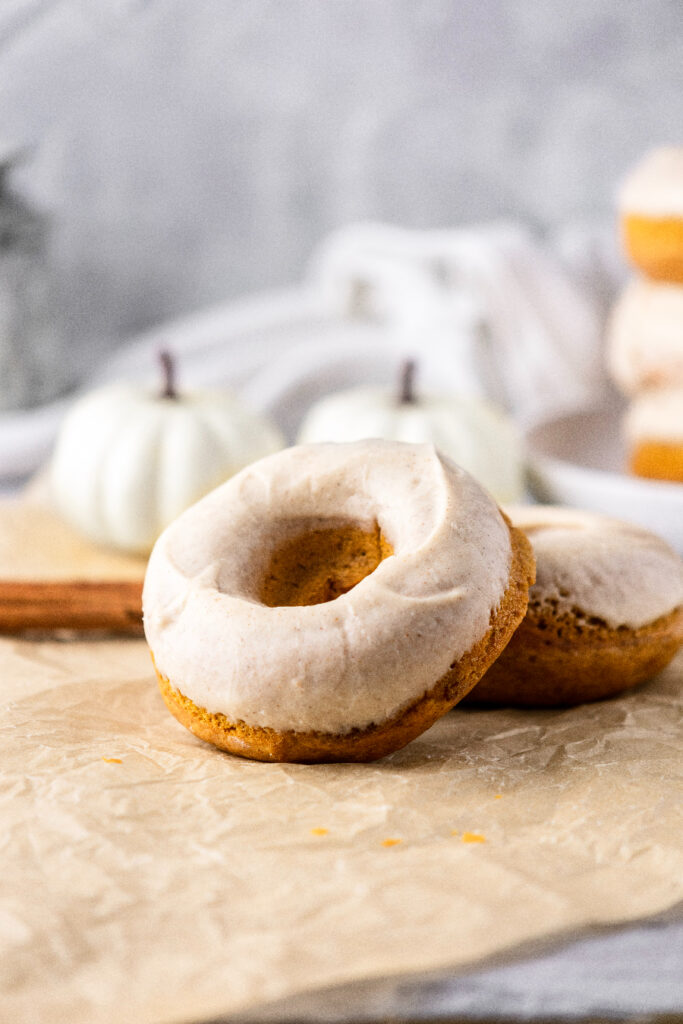 Pumpkin spice donuts with cinnamon glaze surrounded by white pumpkins.