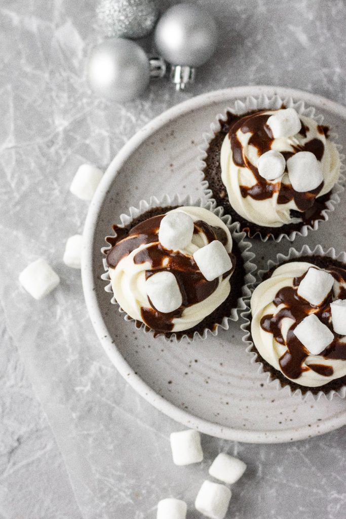 Hot chocolate cupcakes with marshmallow frosting on top sitting on a white plate.