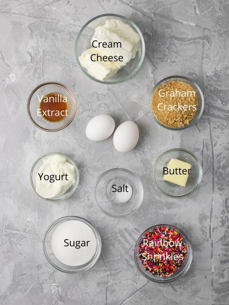 ingredients needed for cheesecake: cream cheese, vanilla extract, graham crackers, eggs, yogurt, salt, butter, sugar, and rainbow sprinkles