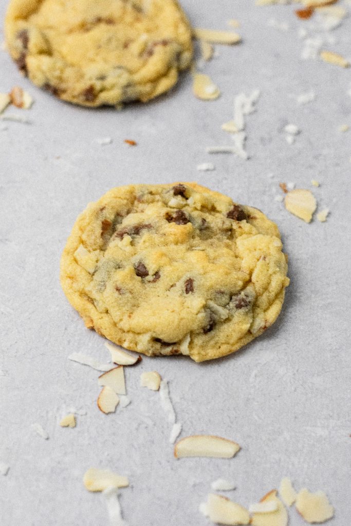 Shredded coconut pieces and almonds around a chocolate chip cookie