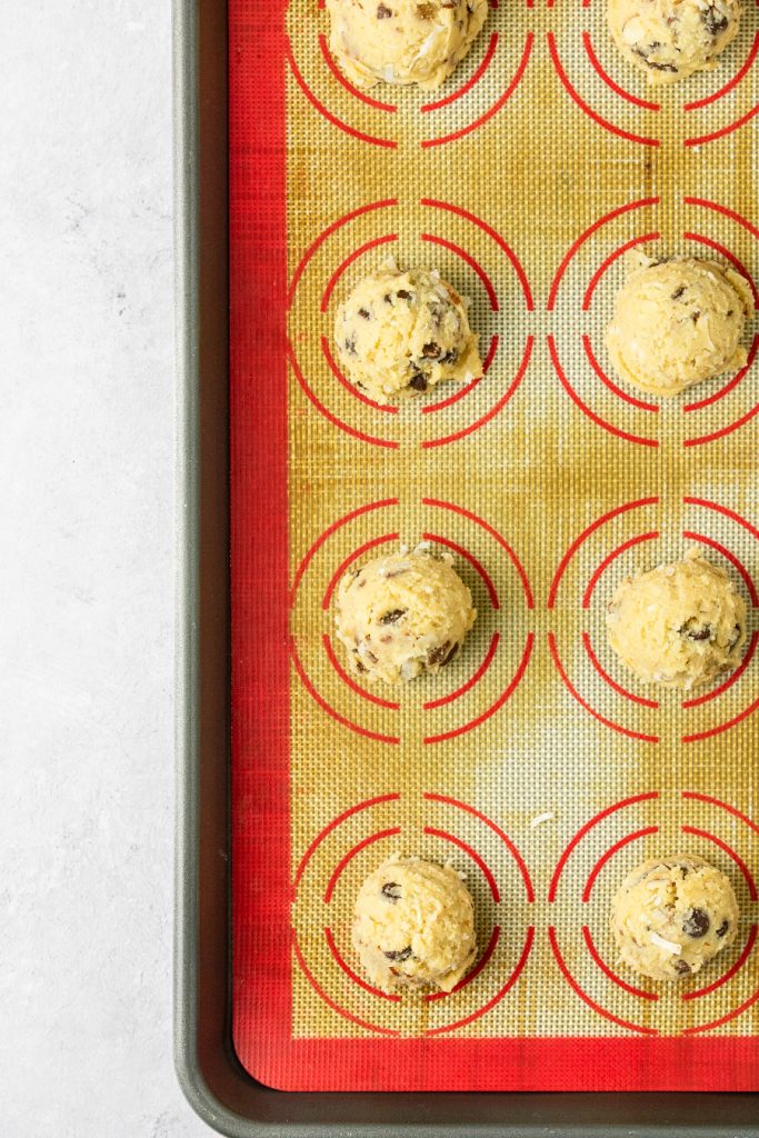 Cookie dough balls ready to bake on a silcone mat lined baking sheet.
