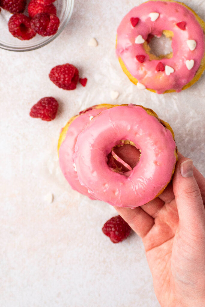 holding a pink donut with raspberries in a bowl.