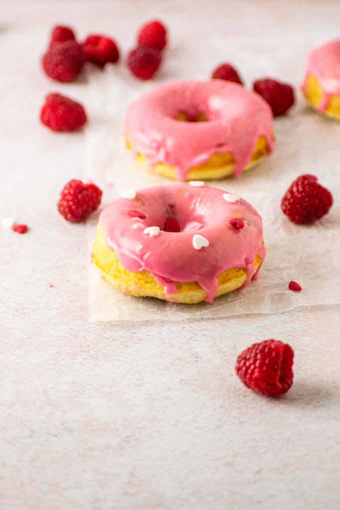 raspberry glaze on top of cake donuts with fresh raspberries and decorated with hearts for valentine's day.