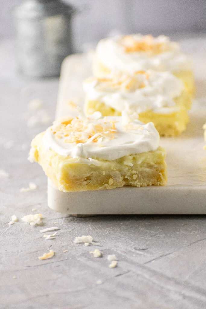 Coconut cream pie bars with toasted coconut on a marble board.