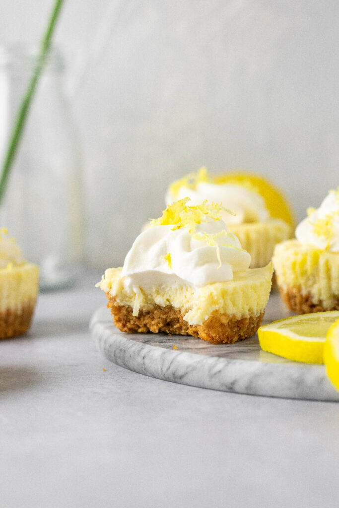 Lemon cheesecake bites with a bite taken out of one that's sitting on a plate.