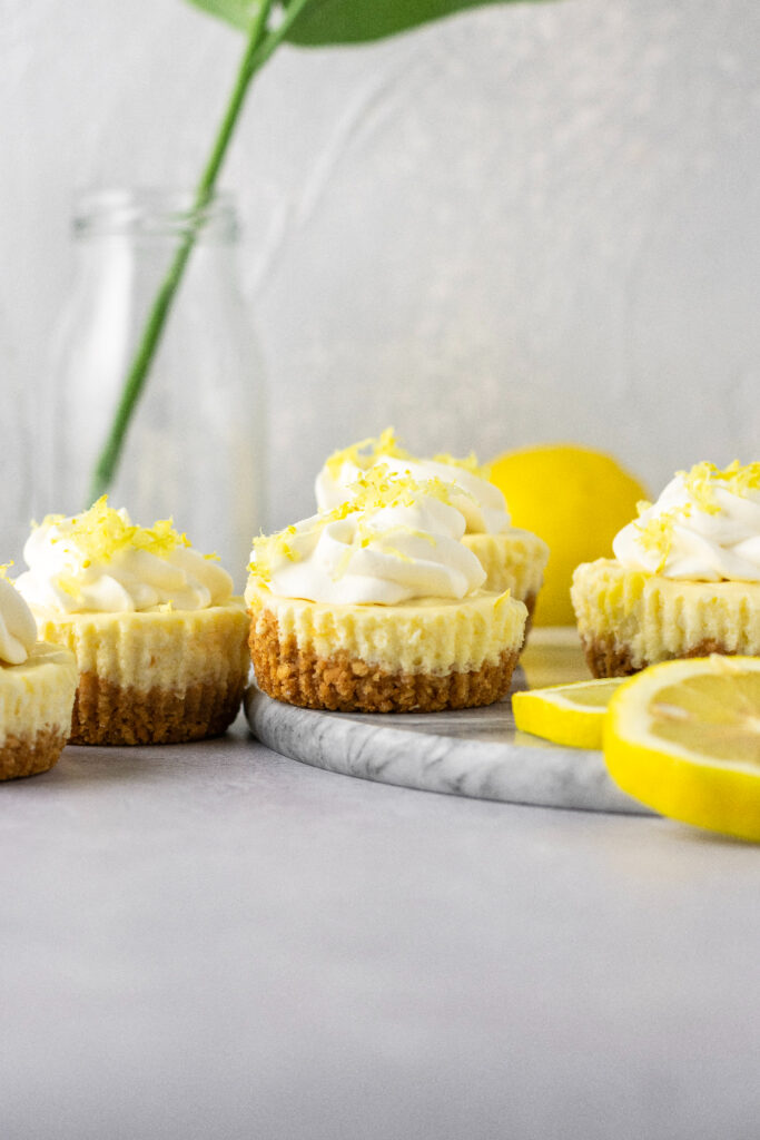 Little cheesecakes sitting on a plate with fresh lemons.