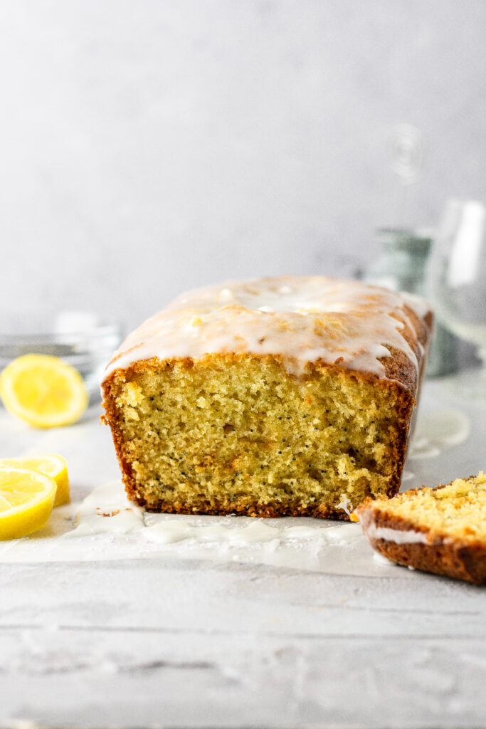 A loaf of poppy seed bread with a sweet glaze on top and some lemons on the side.