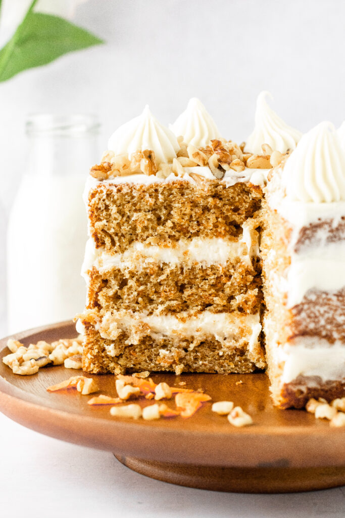 The inside of a carrot cake with walnuts decorated on the top and a jug of milk in the background.