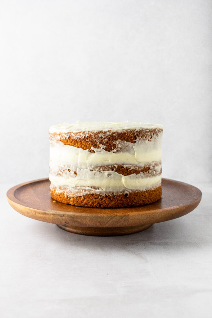 A crumb coated carrot cake sitting on a cake stand.