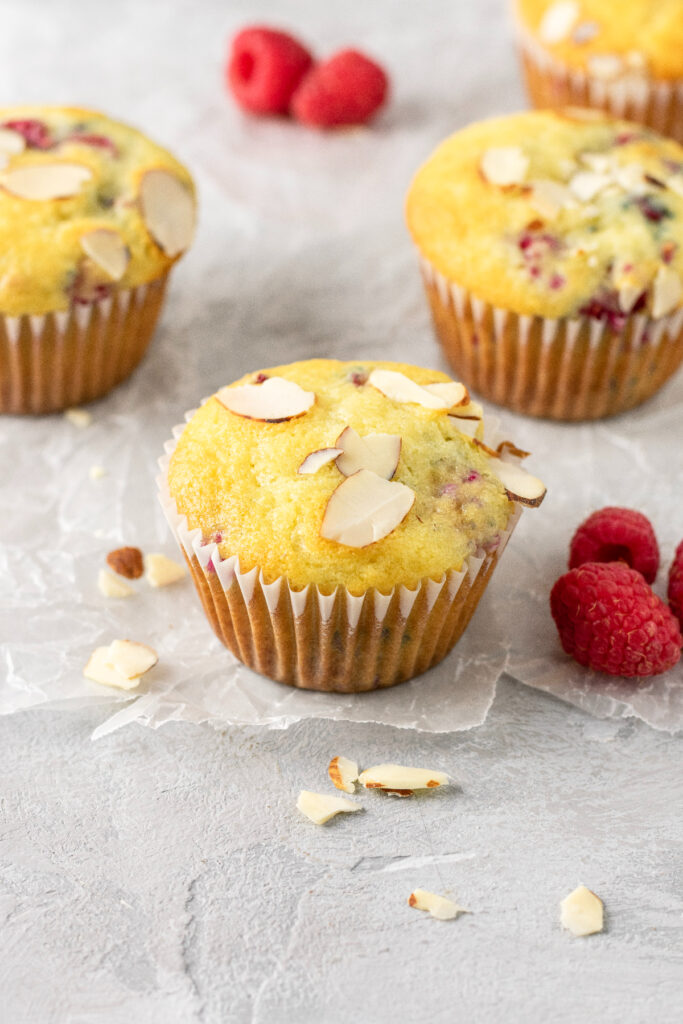 Sliced almonds on top of golden muffins with raspberries.