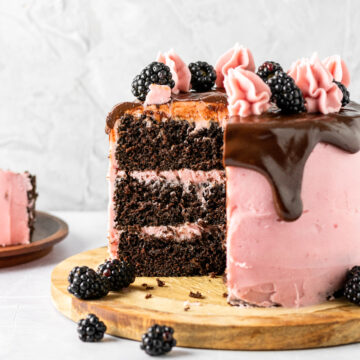 Three layered chocolate cake with blackberry frosting, fresh blackberries, and a chocolate drip.