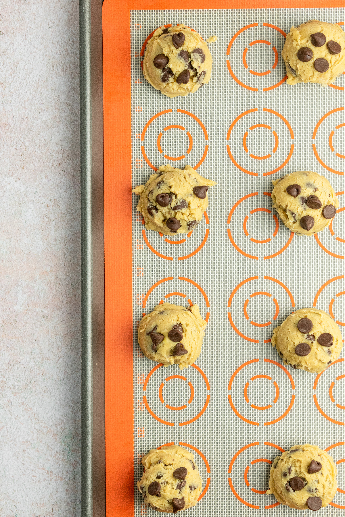 Cookie dough balls on a baking sheet with an orange silicone baking mat