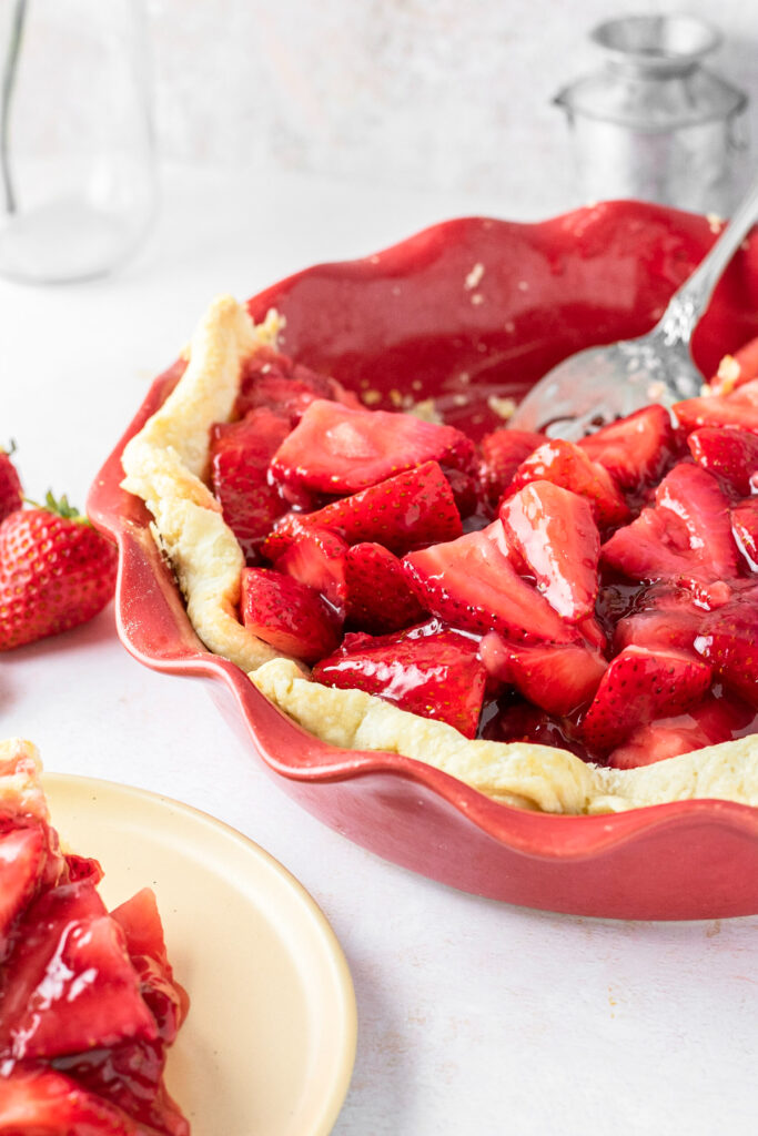 Pie plate with strawberries and plates on the side.