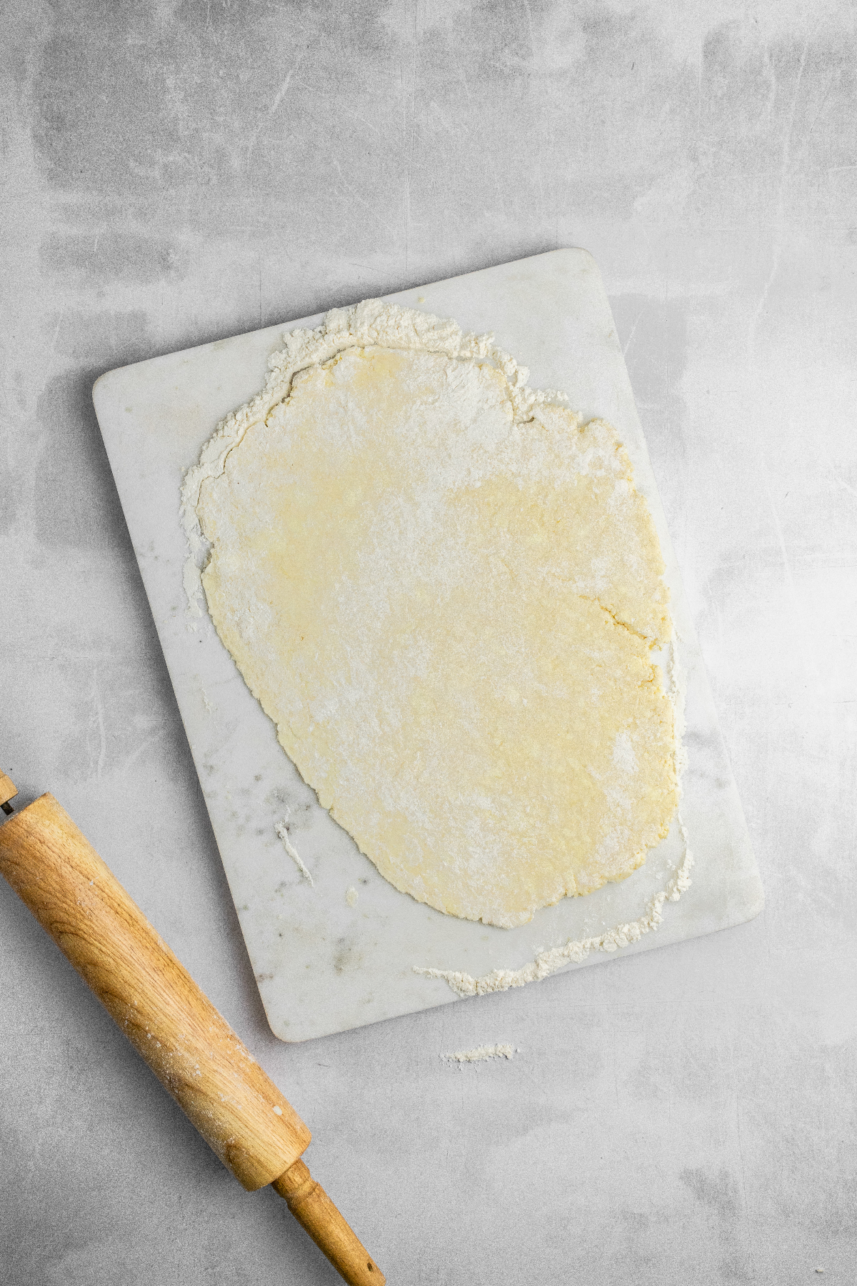 Pie crust rolled out with a rolling pin on a floured surface.