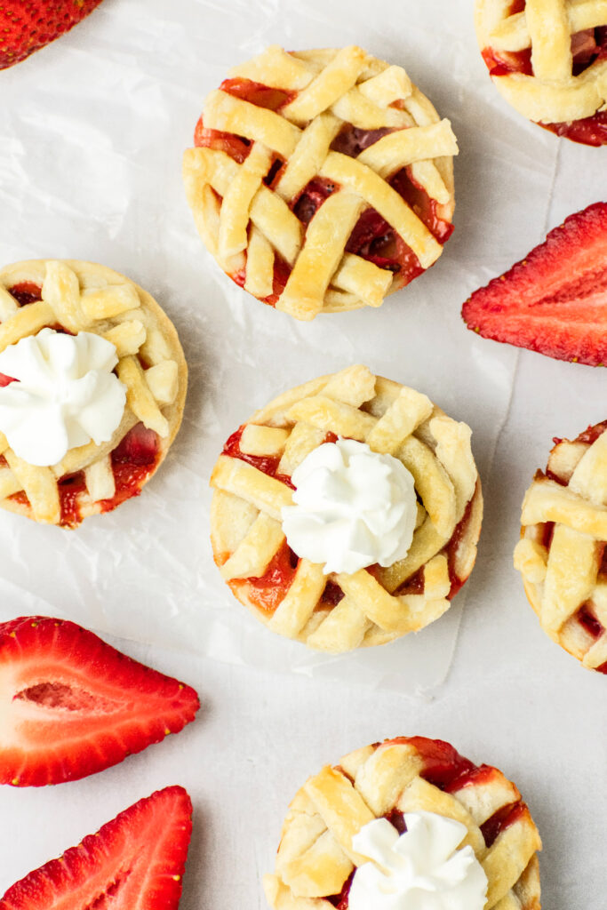 Lattice pie crust on individual pies. Some are topped with whipped cream.