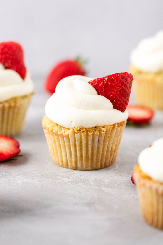 Fresh strawberry cupcakes with whipped cream and strawberries in the background.