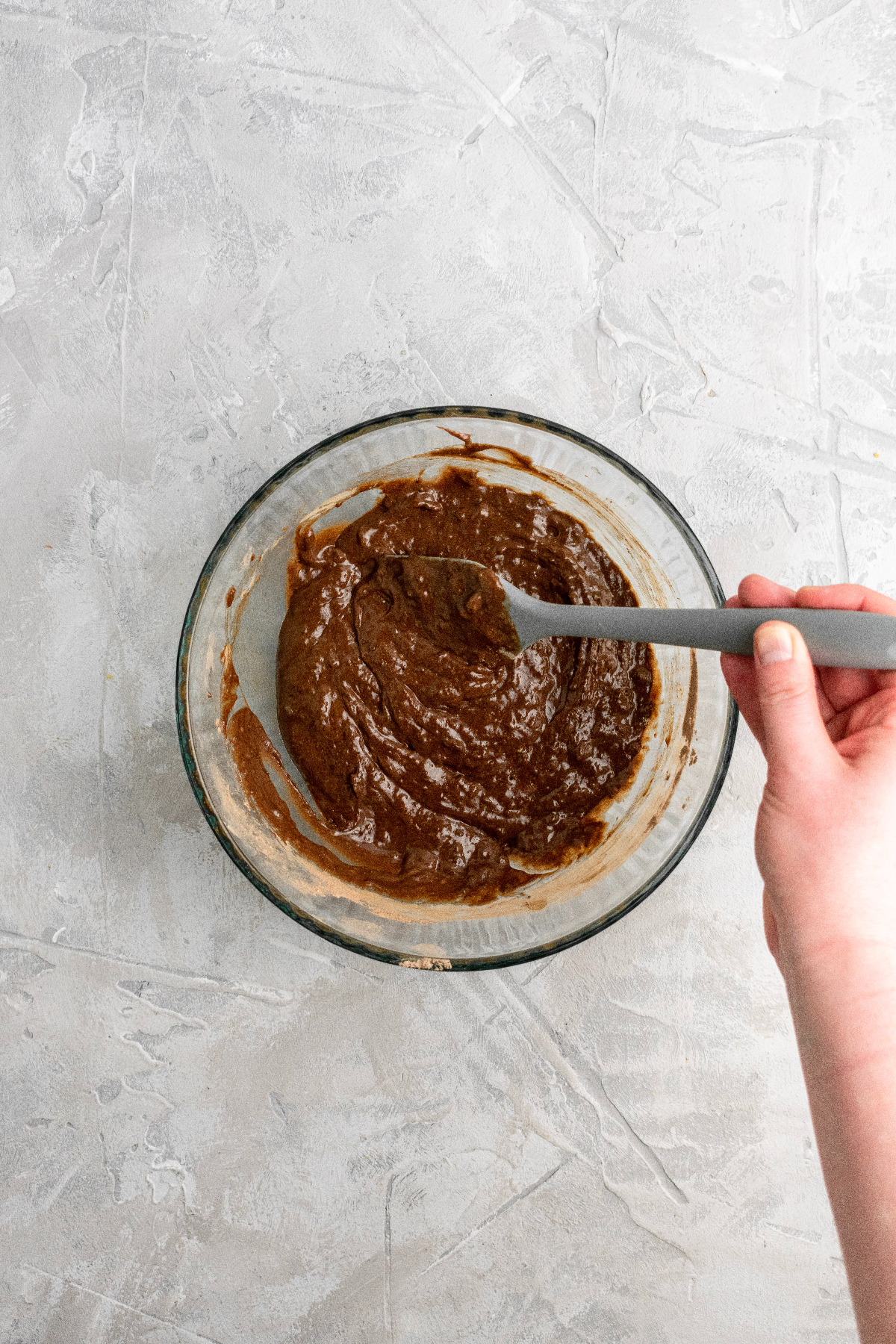Chocolate donut batter in a large bowl being mixed with a silicone spatula.