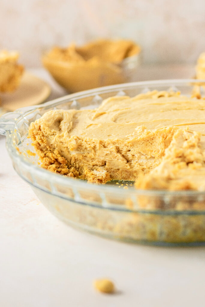 Peanut butter pie with a slice cut out of it and creamy peanut butter in a bowl.