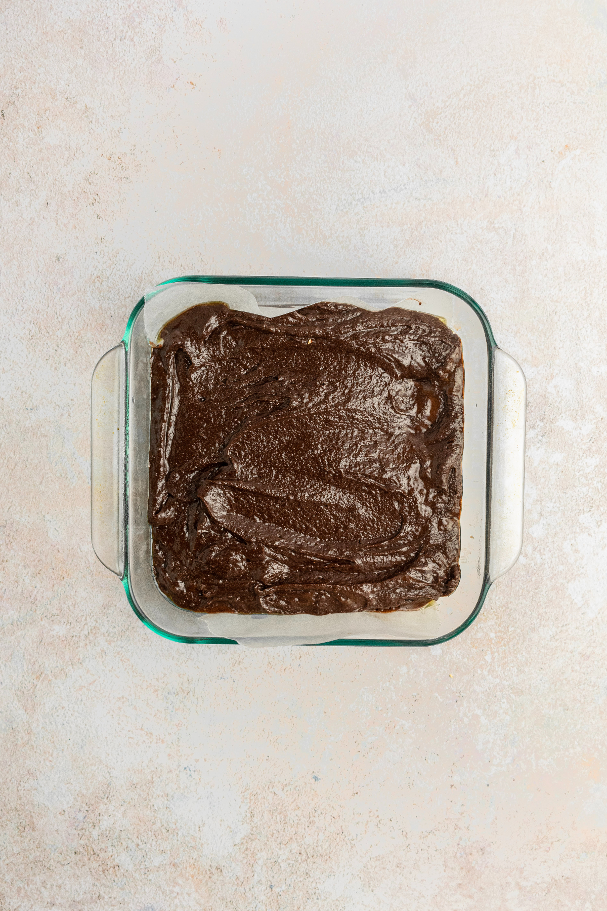 Smoothed out brownie batter in a glass baking pan.
