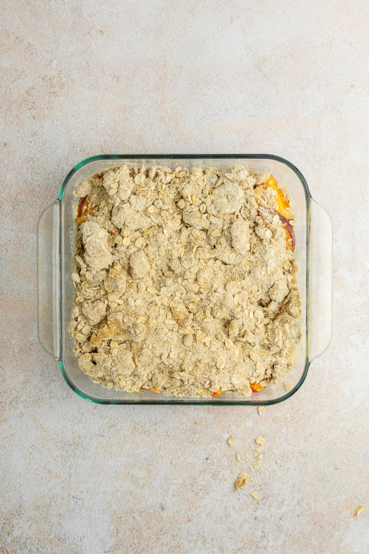 Crisp topping over the peach filling in a baking pan.