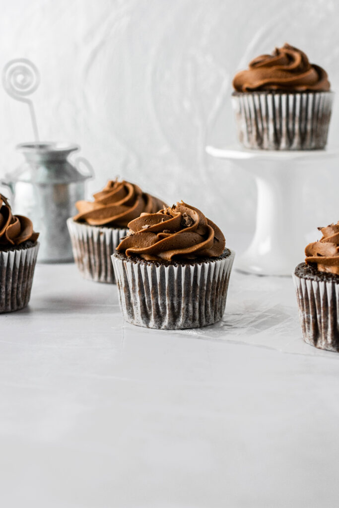 Triple chocolate cupcakes with one sitting on a small white cake stand.