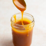 Caramel drizzling from a spoon into a glass jar.
