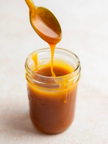 Caramel drizzling from a spoon into a glass jar.