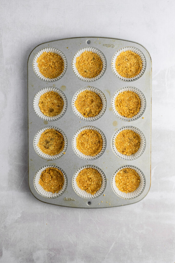 Muffin pan filled with 12 cupcake liners and a graham cracker crust.