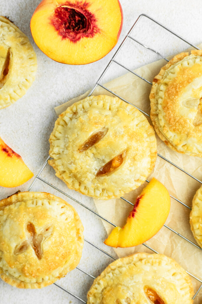 Peach hand pies with fresh peaches and parchment paper underneath.