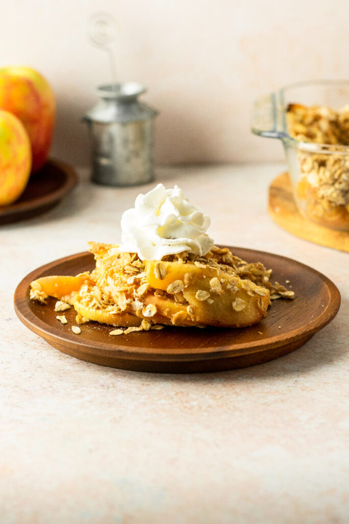 Baked apple crisp on a plate with fresh apples.