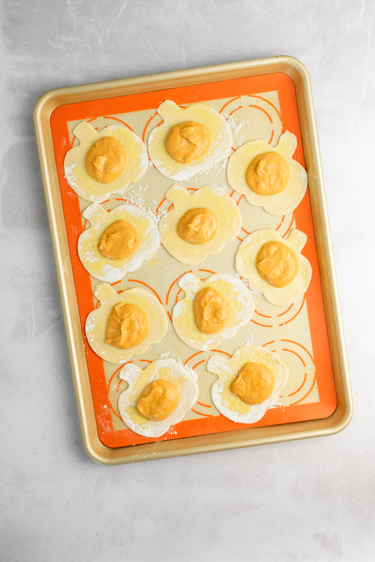 Baking sheet with 10 pumpkin pie doughs with filling.