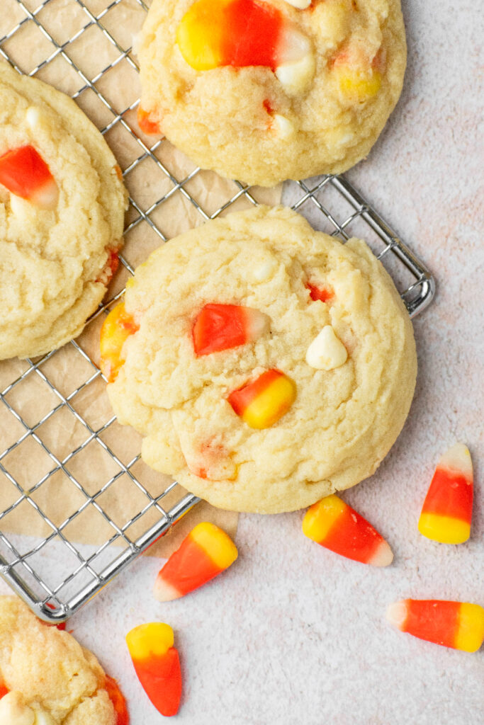 Sugar cookies with white chocolate chips and candy corn sitting on a wire rack.