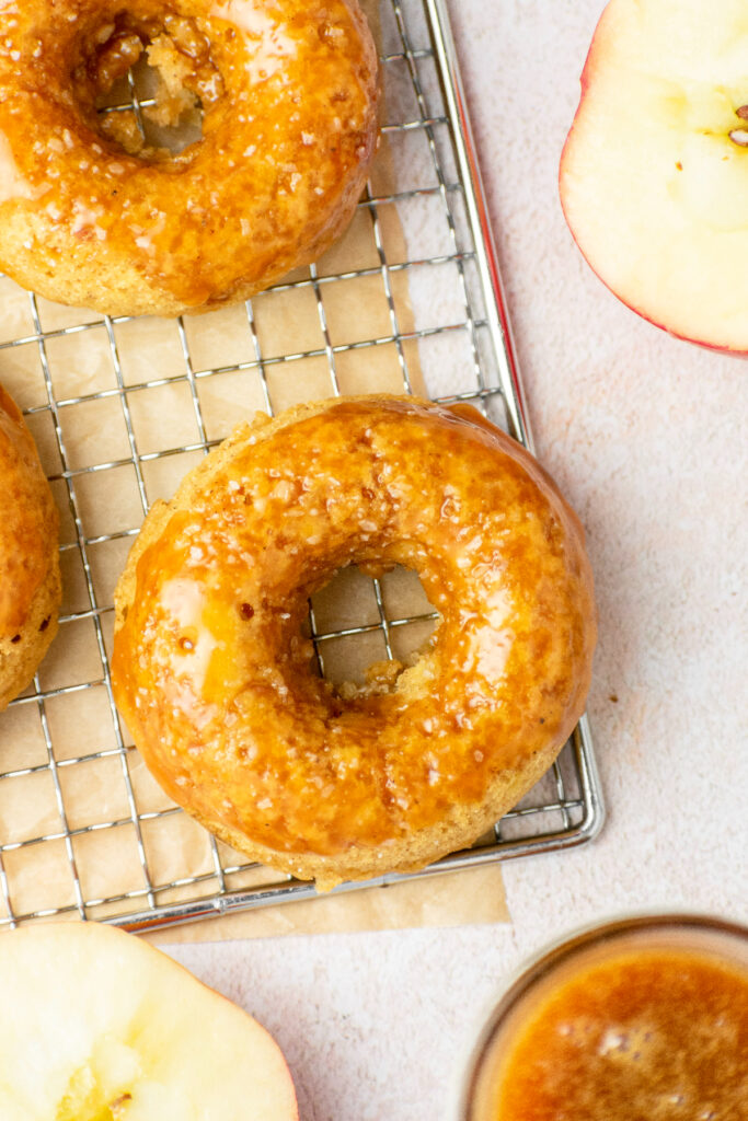 Caramel apple baked donuts on a wired rack with honey crisp apples and more caramel.