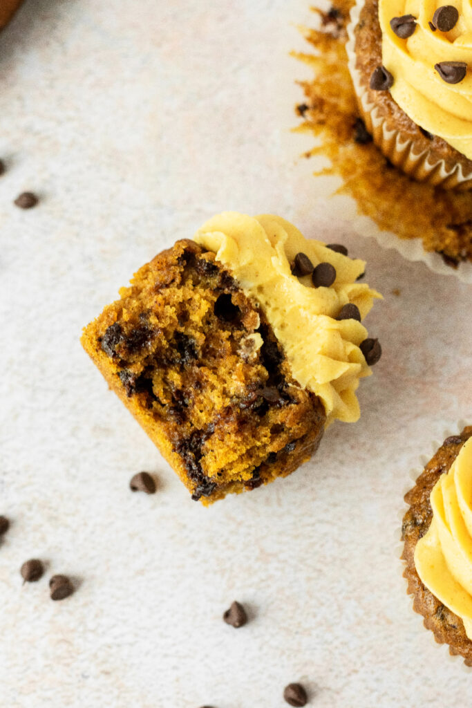 A chocolate chip pumpkin cupcake laying on it's side with chocolate chips all over and a bite taken out of it.