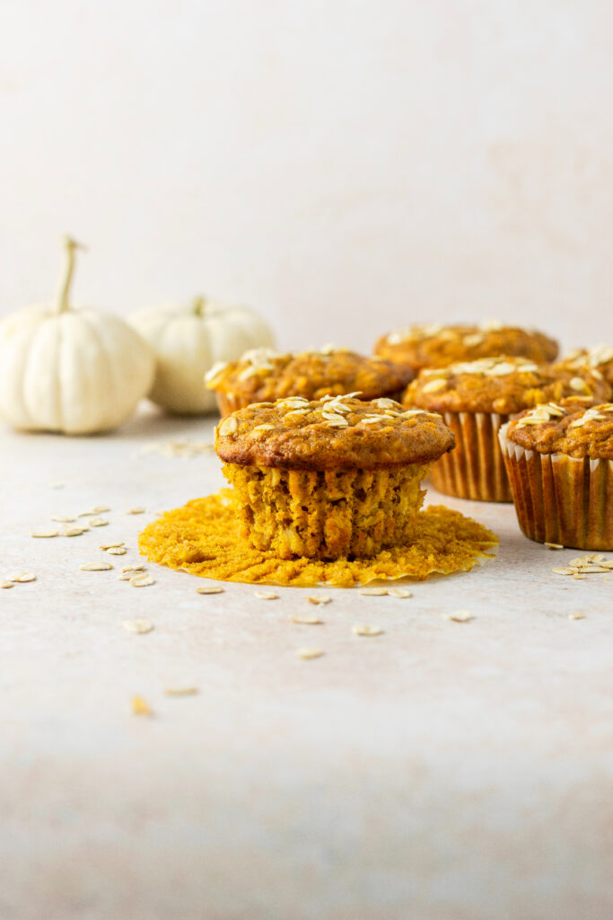 Pumpkin oatmeal muffins with oats on the side and white pumpkins in the back.