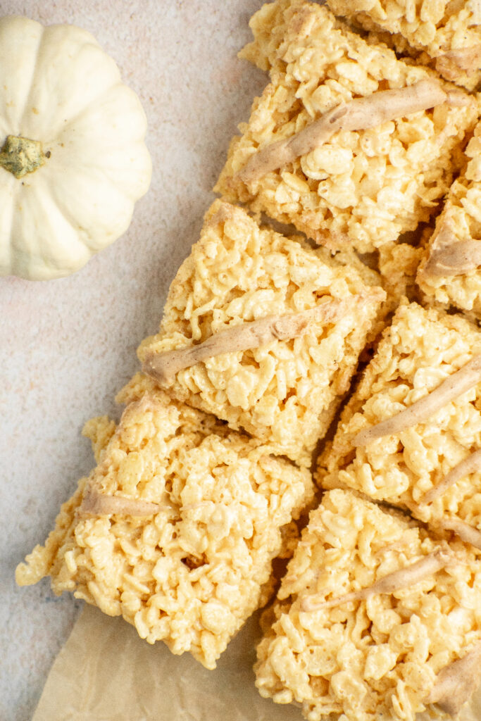 Pumpkin rice krispie treats with a drizzle and white pumpkins on the side.