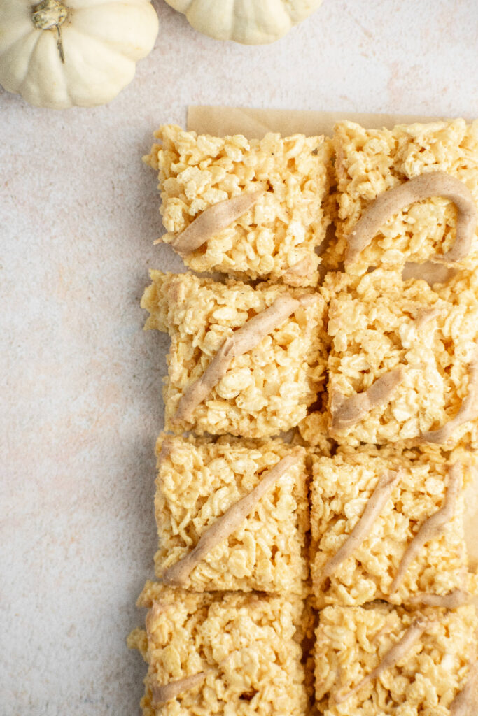 Two rows of pumpkin rice krispie bars with white pumpkins on the side.