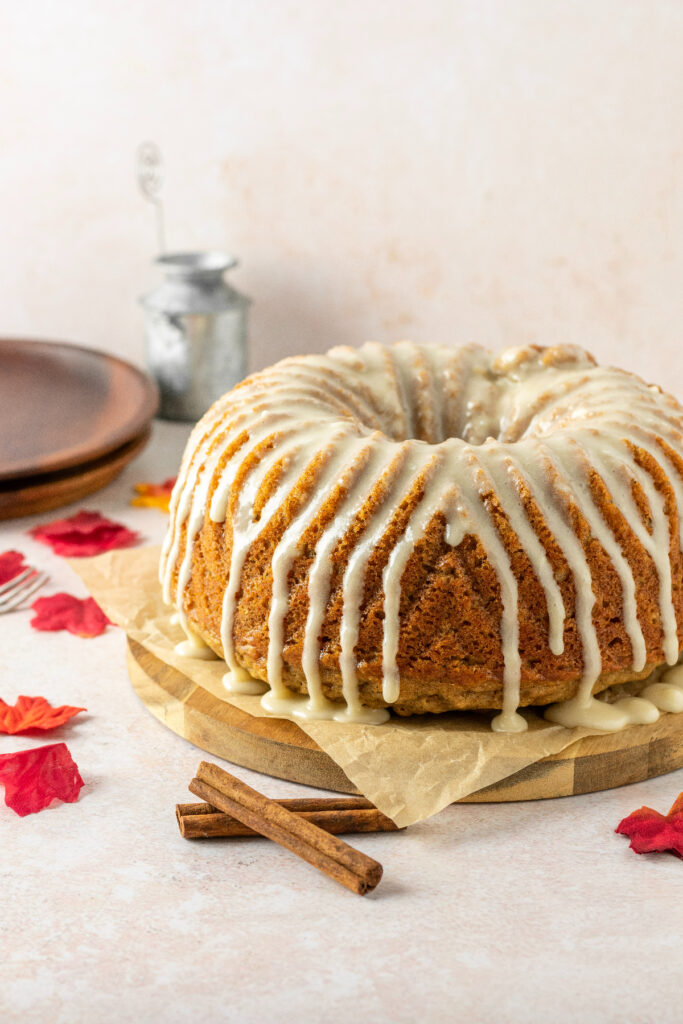 Spice bundt cake with glaze dripping down the side. Brown plates are off to the side and red leaves.