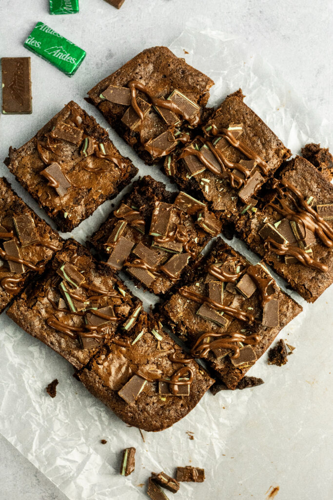A table of brownies on parchment paper with extra andes mint candies on the side.