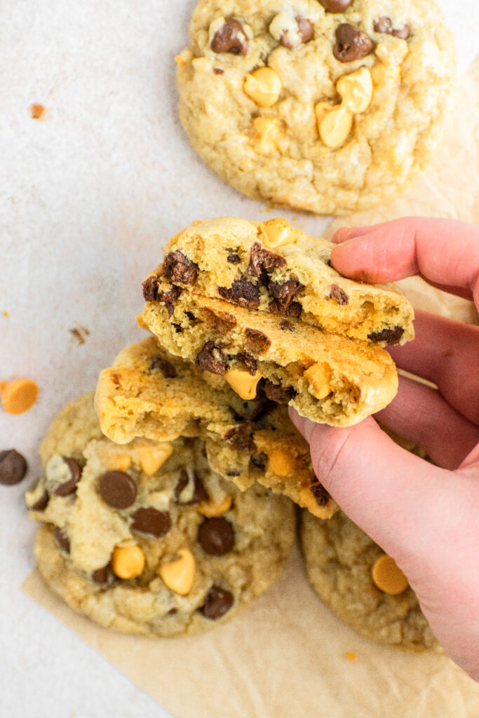 A hand holding chocolate chip butterscotch cookies with the cookies split in half.