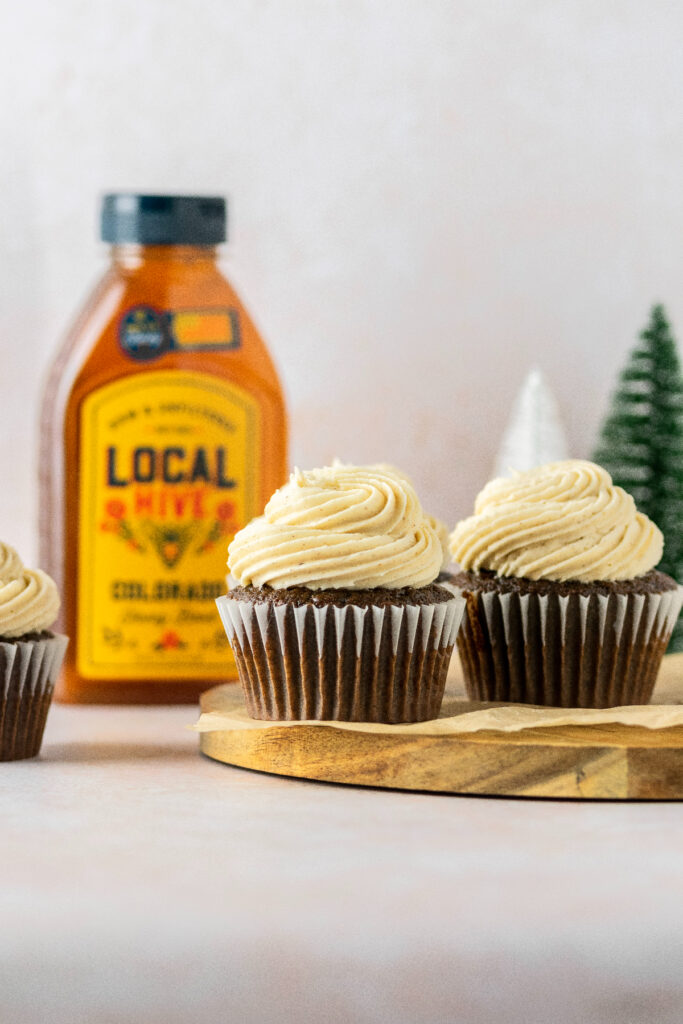 Gingerbread chocolate cupcakes on a brown cake stand with a bottle of honey in the background.