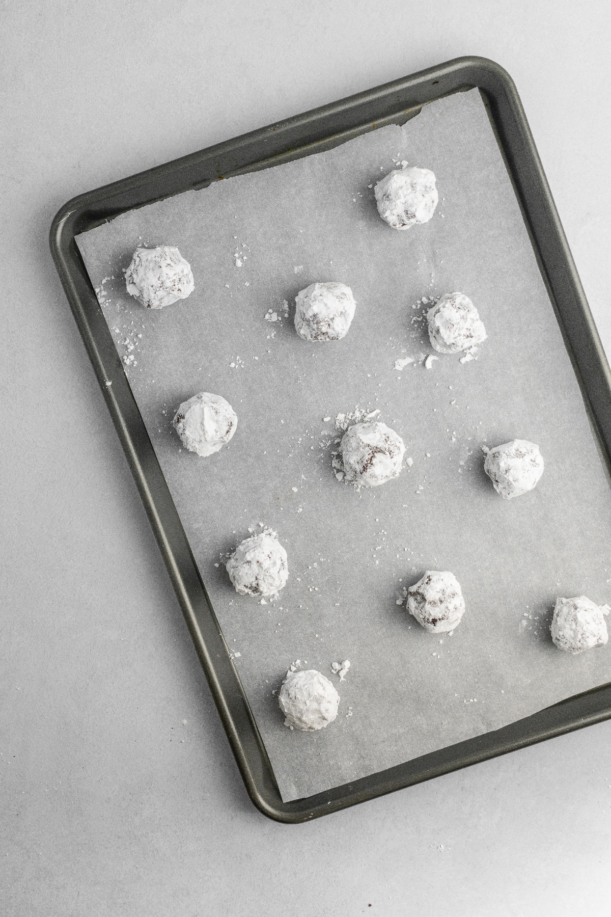 Powdered sugar coated cookie dough balls on a parchment lined cookie sheet.