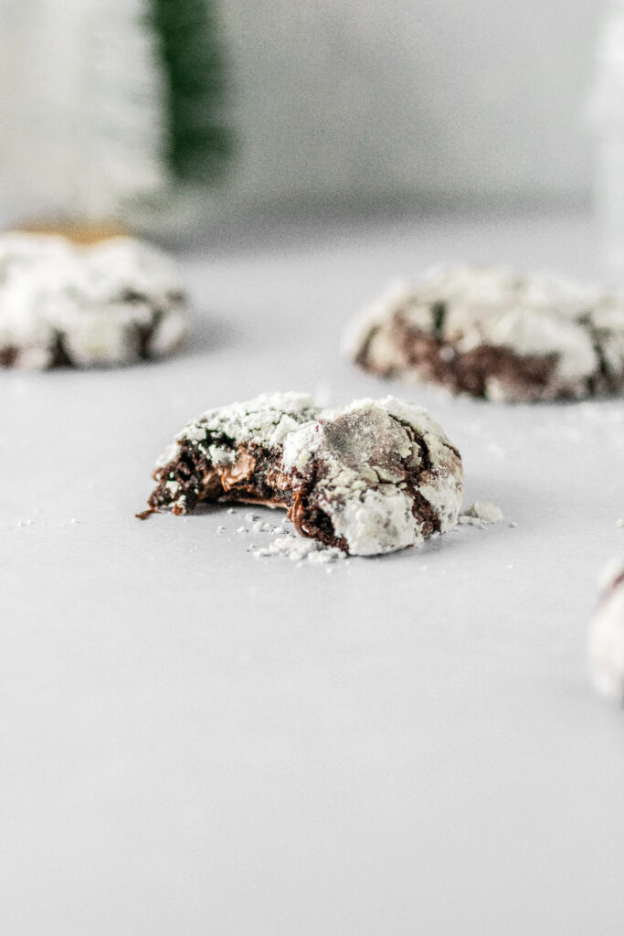 Chocolate crinkle cookies with melty chocolate chips coming out of the bite that was taken.