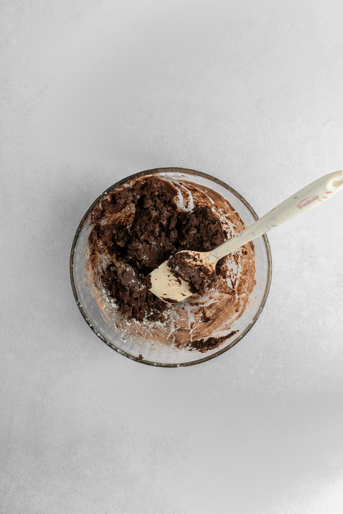 Chocolate cookie dough in a glass bowl with a silicone spatula.