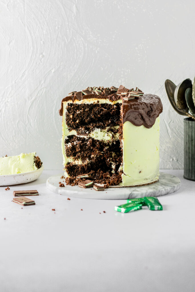 Chocolate mint cake with andes mints, sitting on a cake plate, and metal spoons in the background.
